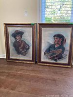 Photo showing both framed canvas paintings side by side on a floor against a wall, allowing appraisal of size, framing, and general condition.
