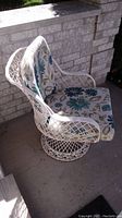 White metal lattice patio chair with floral cushion facing sideways showing armrest and cushion pattern