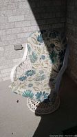 White metal patio chair with floral cushion partially in sunlight against brick wall background.