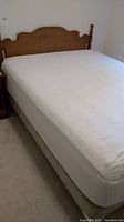 Queen bed with white mattress and wooden headboard from left side angle