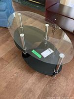 Full view of oval-shaped glass coffee table with metal legs and black base on the floor.