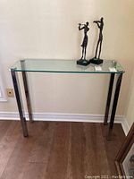 Full view of glass top side table with two decorative metal sculptures on top (not included).