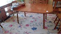 Wooden dining table on floral carpet showing full view from corner angle