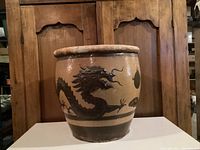 Front view of large antique Chinese jar with a black dragon motif, thick rim, and aged patina.
