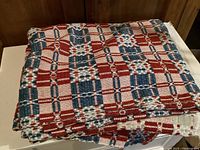 Folded wool coverlet showing red, blue, and white plaid woven pattern.