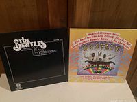 Photo showing The Beatles 1st Live Recordings Volume Two and Magical Mystery Tour album covers leaning against a wooden wall.