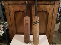 Front view of both cricket bats placed side by side showing player names and brands.