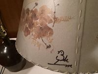 Close-up of signed floral lamp shade with pressed botanical designs and stitched edges.