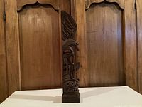 Front view of the tall, carved wooden sculpture showing bird and facial motifs.