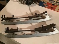 Close-up photo of two vintage steel ice skate blades showing metal construction and mounting brackets.