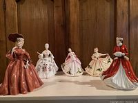 Group of five porcelain figurines on display, front view showing dress details and posing