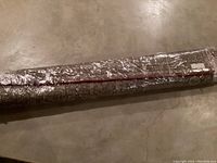 Rolled vintage area carpet wrapped in clear plastic wrapping on concrete floor