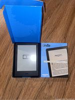 Amazon Kindle e-reader with screen showing error, original box, and user manual laid out on wooden floor.