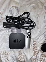 Photo of Apple TV device, remote, and power cord on fabric surface with postal print.