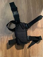 Top view of black tactical leg holster with straps laid out on wood floor.