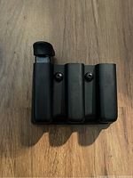 Front view of black triple magazine holder with three compartments and one magazine partially inserted.