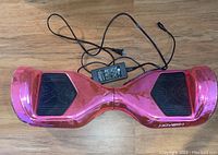 Top view of pink hoverboard with black footpads and charger cable placed on wooden floor.