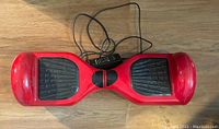 Top-down view of red hoverboard showing black footpads and included charger cable on wooden floor