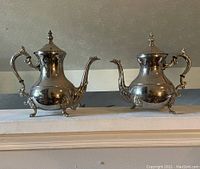Photo of silver-plated coffee pot and teapot set on mantle showing missing leg on coffee pot and overall tarnish.
