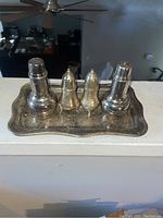 Silver tray with four silver shakers arranged on top, showing overall set condition and scratches.