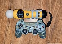 Photo showing yellow Wii Motion Plus controller and camo PlayStation 3 controller together on a black surface