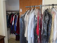 Full view of clothes on hangers and rack showing a variety of men's and women's clothes including suits, shirts, and sweaters many in dry cleaning bags.