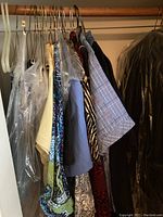 Hanging women's and men's clothing including suits and dress blouses, some garments with plastic dry cleaning covers.