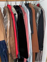 Closely packed ladies coats, jackets, and dresses on hangers including leather, wool, and fur trim varieties