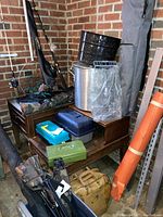 Overview of lot showing tackle boxes, cooking pots, fishing rods and carry bags on a wooden stand against brick wall