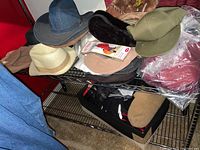 Overview of assorted men's hats including fedoras, caps, berets, and folded winter gloves on metal shelves.