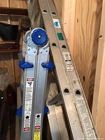 Two aluminum ladders standing side by side: Werner 16-foot extension ladder and Costco multi-positional ladder with blue knobs and handles.