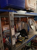 View of metal shelving unit with assorted boxes and items including a white fan on middle shelf.