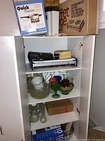 Cabinet interior with stacked small appliances and glassware items.