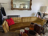 Full view of the gold upholstered sofa with a red pillow on the left side, positioned below a large ornate mirror.