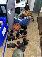 Photo of multiple adjustable dumbbells with black metal plates, a Spalding NBA basketball, and a blue laundry basket containing snorkels and fins, with two wooden tennis rackets leaning against the basket.