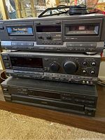 Stacked stereo components showing dual cassette deck on top, receiver in the middle, and CD changer at the bottom.