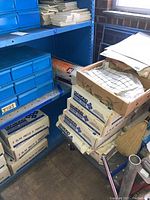 Multiple boxes of white square 12x12 tiles stacked with some other materials and a blue cabinet nearby.