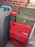 Full view of red metal rolling tool chest with multiple drawers with two smaller toolboxes and other tool containers on top.
