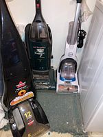Three floor cleaning machines: Bissell ProHeat carpet cleaner, Hoover WindTunnel vacuum, Hoover Power Dash floor cleaner in a corner.