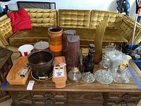 Wide view of lot on wooden table including vases, totems, baskets and glassware in front of green velvet couch