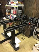 Two adjustable dumbbells with multiple round weight plates sitting on and next to a black metal dumbbell stand in a basement room with wood panel walls.