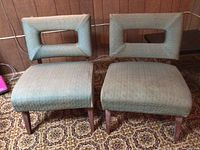 Two modern-styled chairs with rectangular open-back frames upholstered in light green patterned fabric with wooden legs, set on a brown patterned carpet.