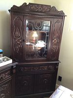 Front view of dark wood china cabinet showing carved floral designs and central glass door with decorative mullions.