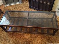 Front angle view of the rectangular wooden coffee table with glass top, showing wear on the wood and carpet flooring.