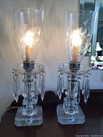 Pair of crystal lamps illuminated with clear glass bases and hanging crystal prisms, topped with etched glass hurricane shades.