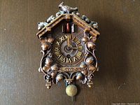 Front view of the wood carved cuckoo clock showing overall design, clock face with Roman numerals, floral carving, bird figure on top, and brass pendulum.
