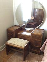 Dresser with large round mirror attached and upholstered bench in front. Furniture shows minimal wear and some scratches.