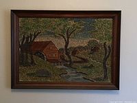 Full view of framed textured landscape art showing a cabin, trees, and a stream in a dark wooden frame.