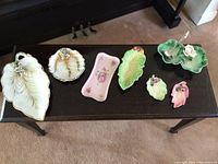 View of seven assorted ceramic serving platters including leaf-shaped and floral designs placed on a black table