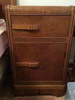 Front view of the wooden side table showing drawer, cabinet door, carved handles, and decorative carved details.